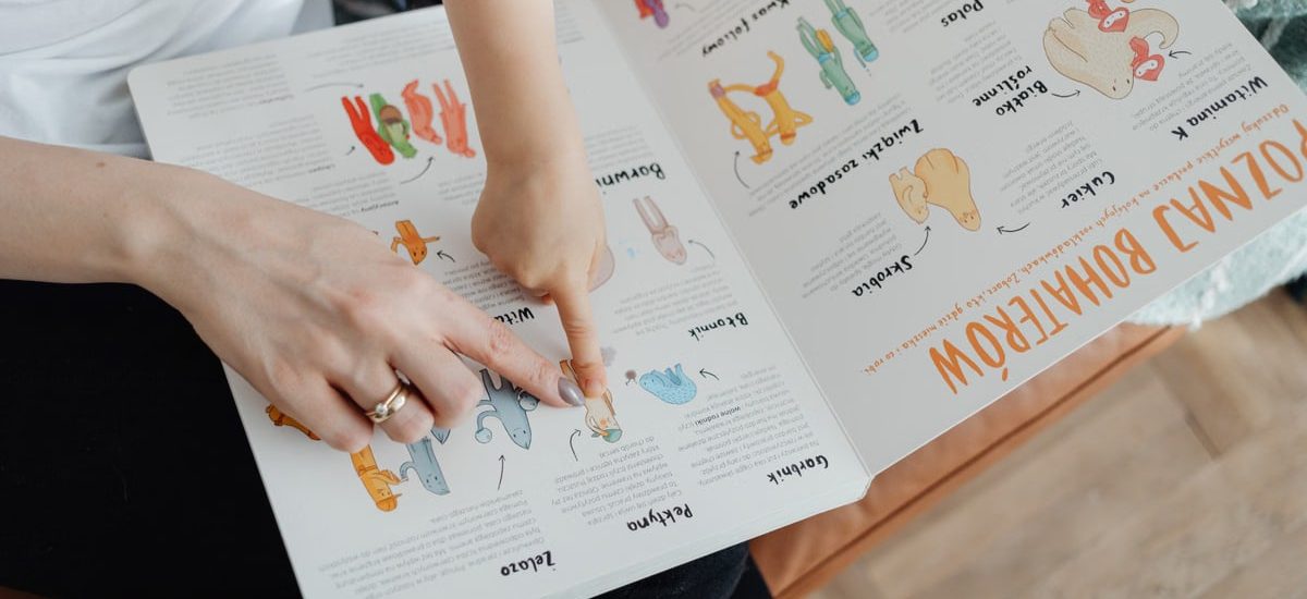 A child and adult engaging with an educational book, pointing to illustrations.