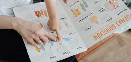 A child and adult engaging with an educational book, pointing to illustrations.