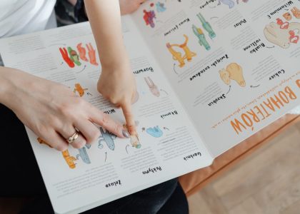 A child and adult engaging with an educational book, pointing to illustrations.